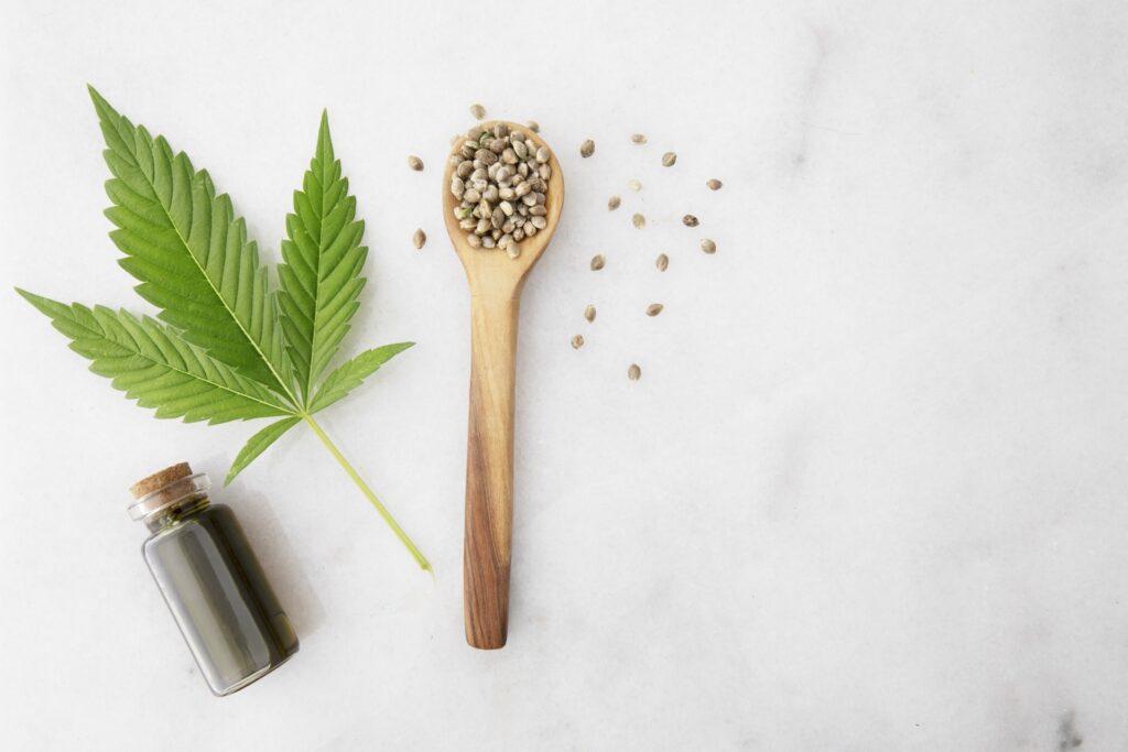 Bottiglietta di olio di CBD con foglie e semi di cannabis in un cucchiaio di legno
